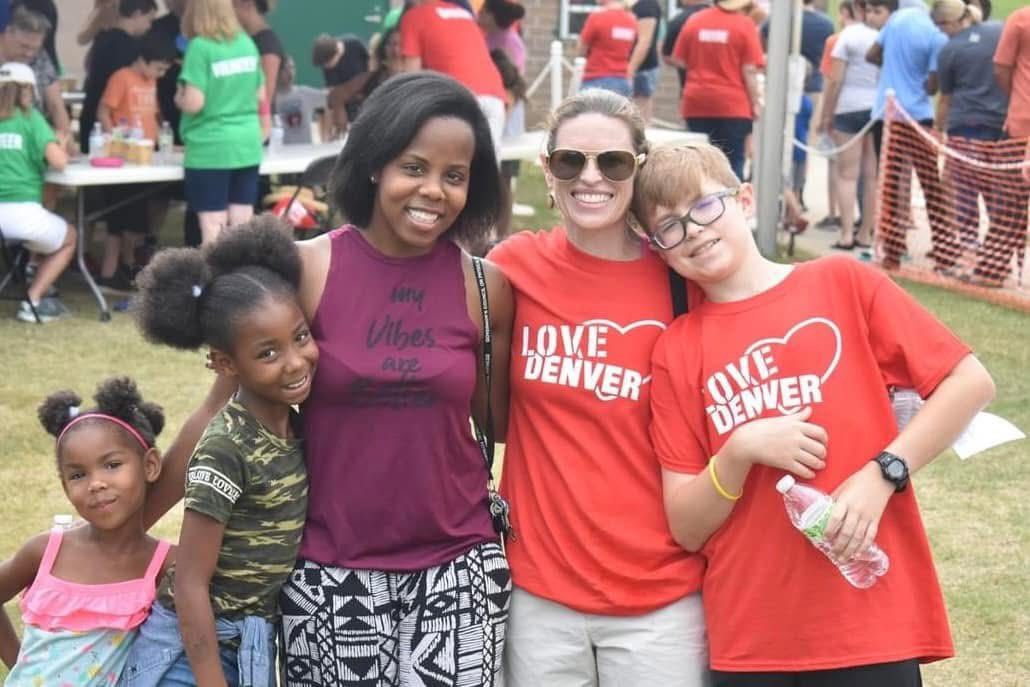 Volunteers in Love Denver shirts hugging a family at a past event